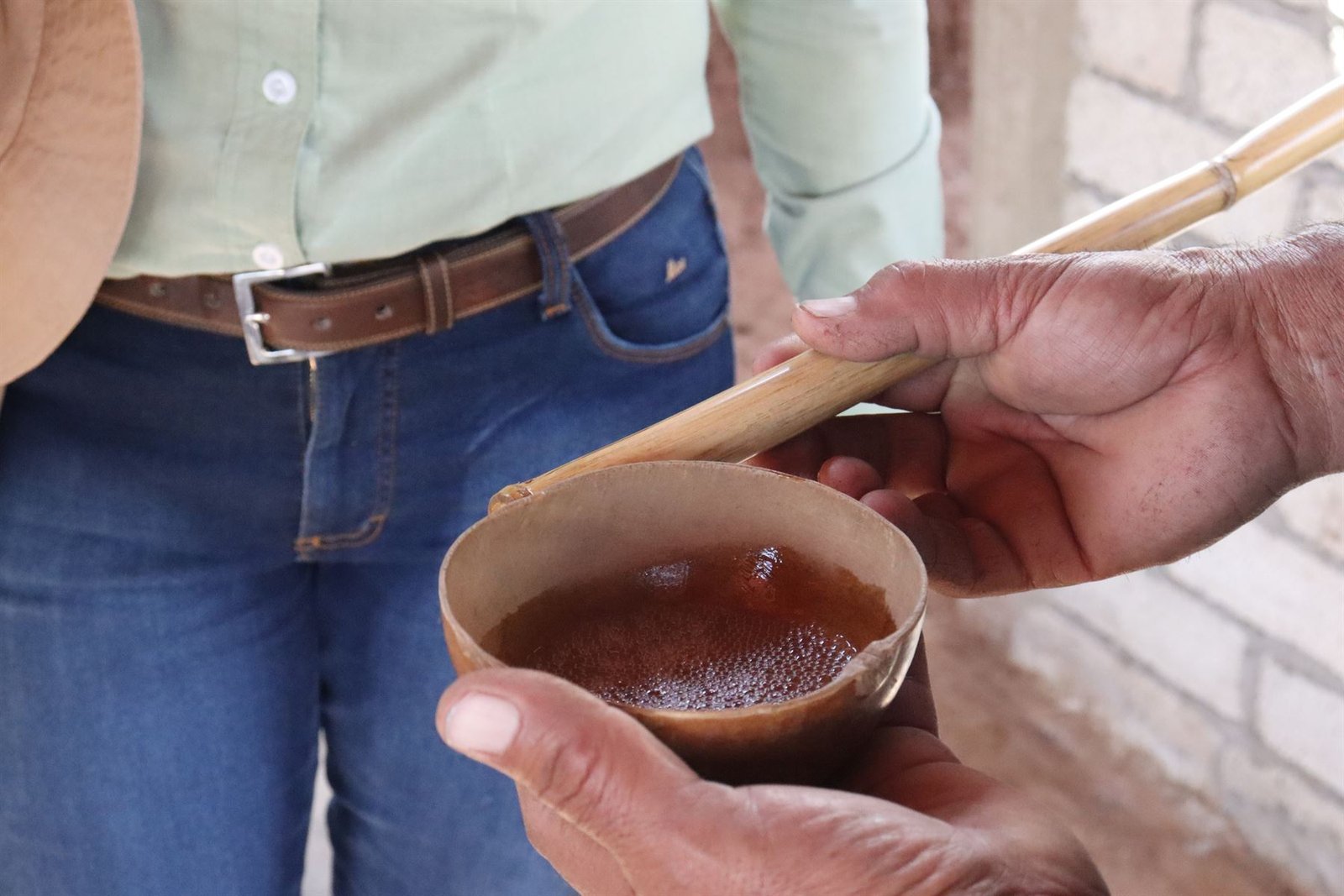 Manos sosteniendo una jícara de barro con mezcal